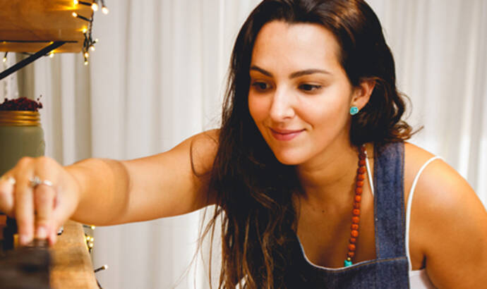 Woman in an apron smiling and reaching for essential oil bottles on a workbench