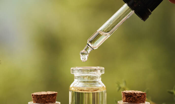 Glass dropper bottle with pipette above two small amber and clear glass bottles of essential oil on a wooden surface"