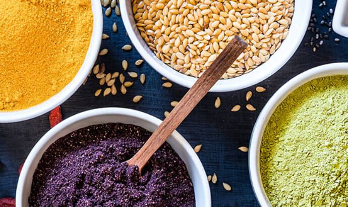 spices and nuts in white bowls with brown spoons stuck in them arranged on a blue tablecloth
