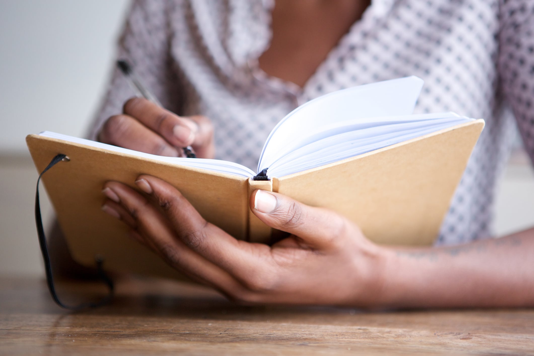 a woman holds a beige notebook with one hand and writes on a page with the other