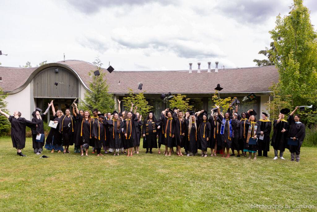 2024 ACHS graduates lined up on the grass throwing their hats in celebration.