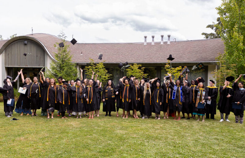 2024 ACHS graduates lined up on the grass throwing their hats in celebration.