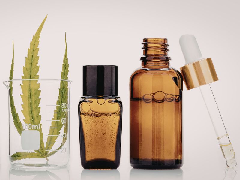 2 bottles of essential oils and a green herb in a glass cup