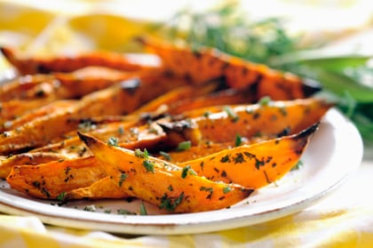 slices of orange vegetables, roasted and covered in herbs, sit on a white plate