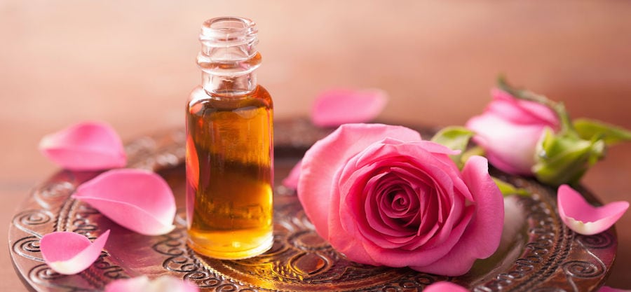 a clear glass bottle of amber liquid sits on a carved plate next to a pink rose