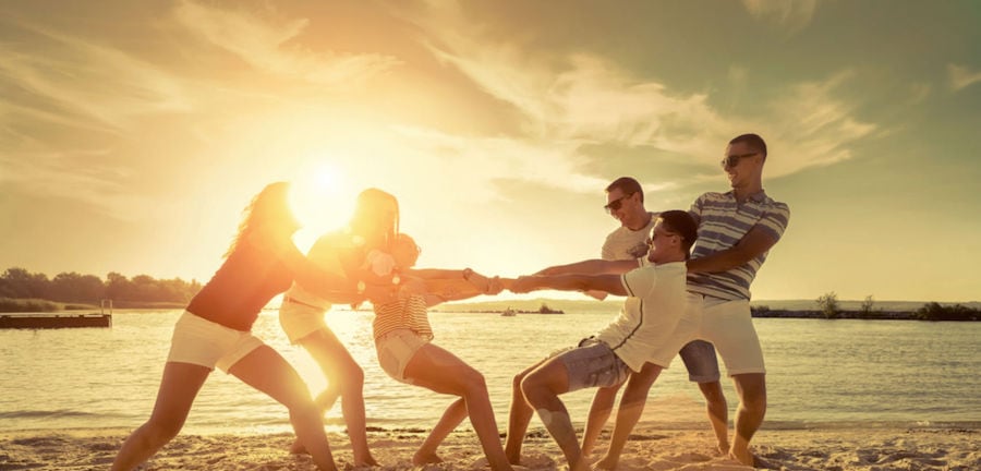 friends funny tug of war on the beach under sunset sunlight.