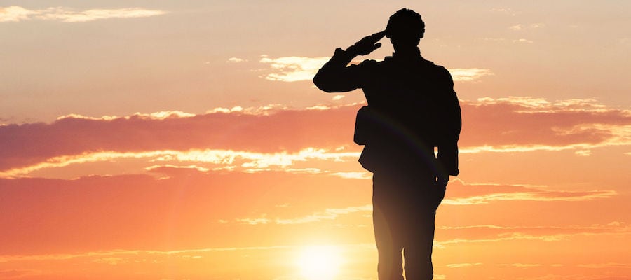 a black silhouette of a person holding their hand to their temple in a salute in front of a orange sunset