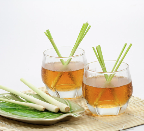 Two short glasses of lemongrass tea with stalks of lemongrass sticking out of them and next to the glasses