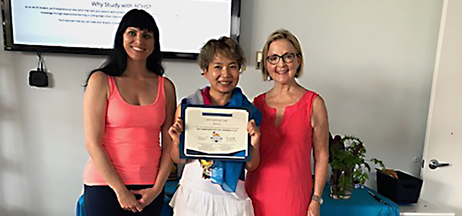 three women smile and looking at the camera, the woman in the middle is holding a certificate up, smiling