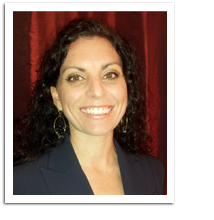 woman with dark curly hair smiles at the camera while standing in front of a red background