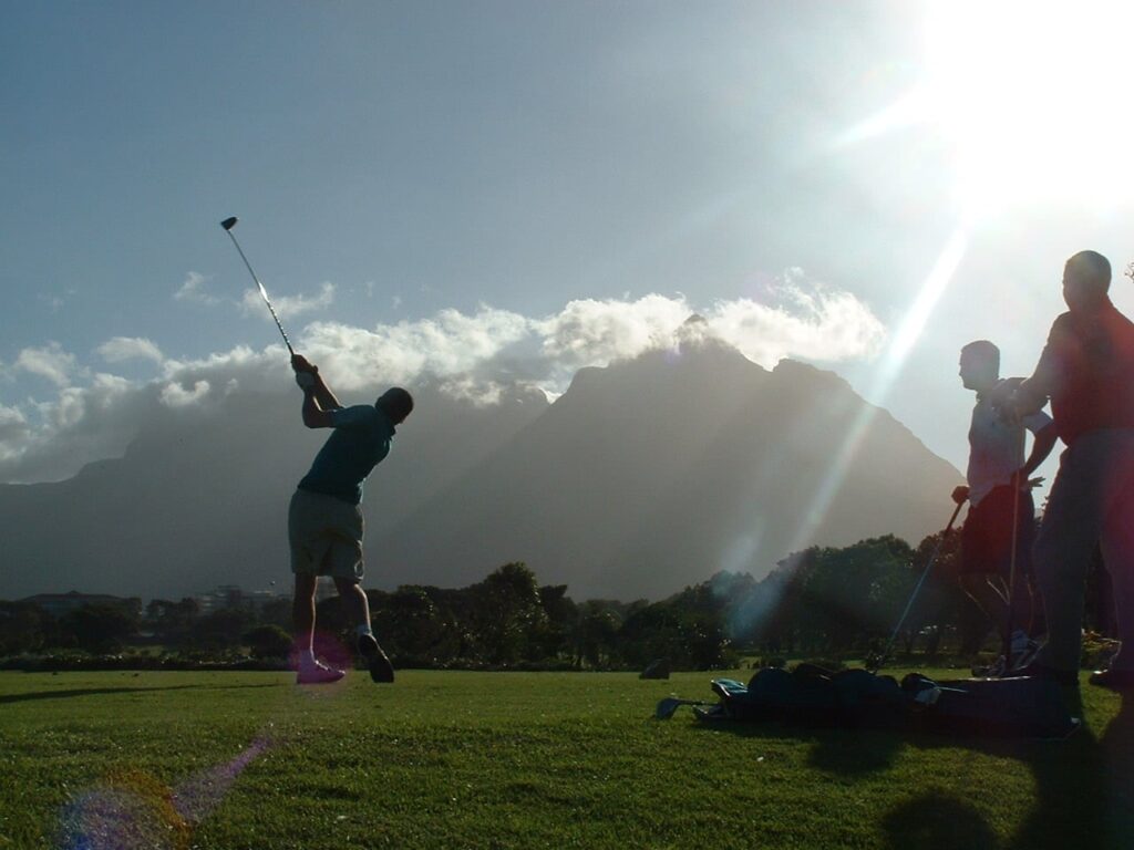 three people are on a golf course, one of them is swinging their club while the other two stand off to the side watching