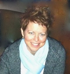 woman with short brown hair wearing a grey cardigan and light blue scarf smiles at the camera