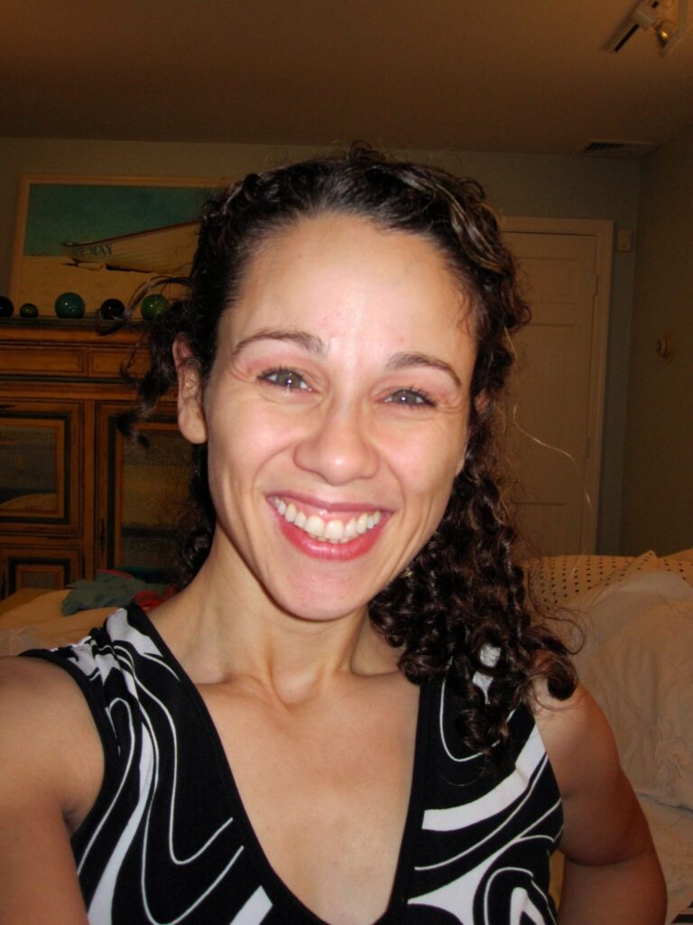 a woman with dark curly hair and wearing a black and white strapless shirt smiles at the camera