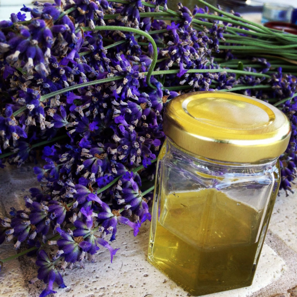 lavender flowers sit on a table behind a small jar of honey-like liquid