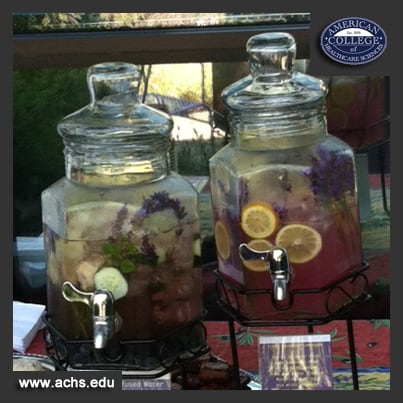 two big glass jars of lavender lemonade on a table, with lavender and lemons floating inside