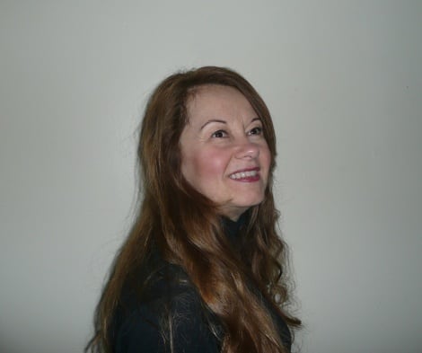 woman with long brown hair looks up and off into the distance, smiling