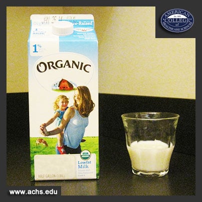 container of milk saying "organic" on it sits on a table next to a clear glass halfway filled with milk