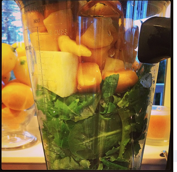 a clear blender holds leafy greens and orange fruit cubes, ready to be blended