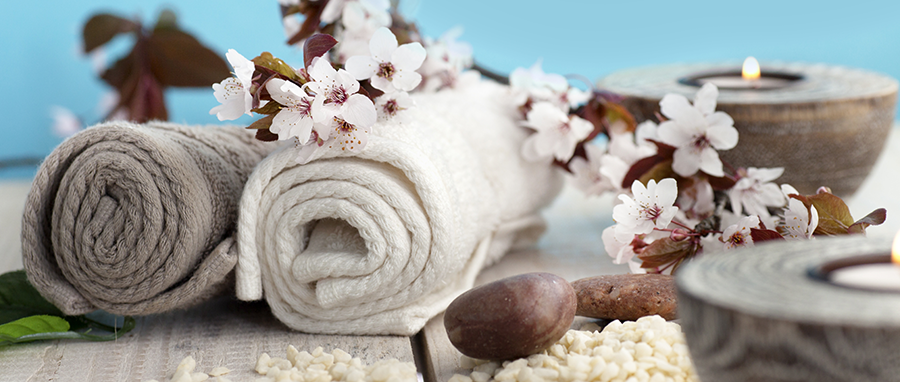 spa towels are rolled up and displayed on a table with white flowers and candles