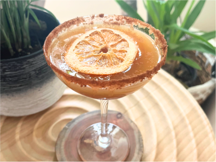 Apple Mock-tini in a glass on a table with green plants behind it