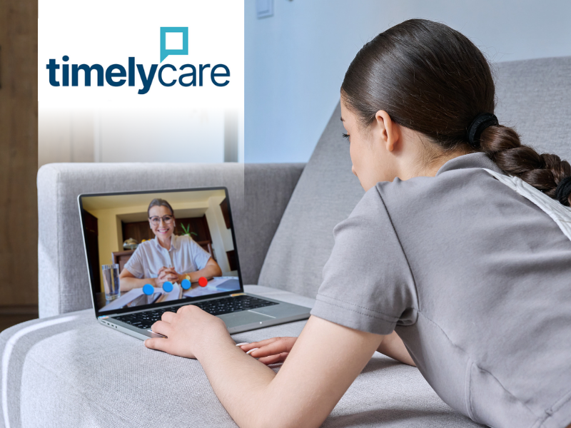 A woman lays on a couch and speaks to a counselor on her laptop