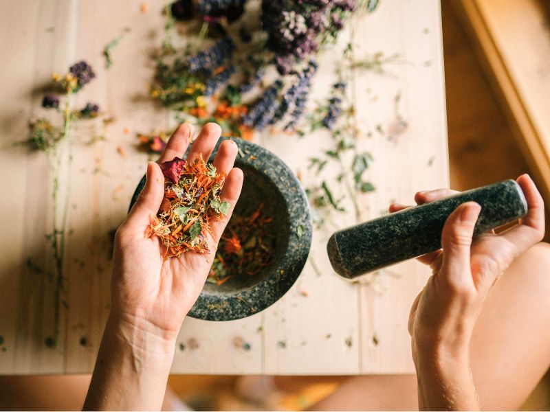 A hand holds colorful fried herbs over a mortar and pestle