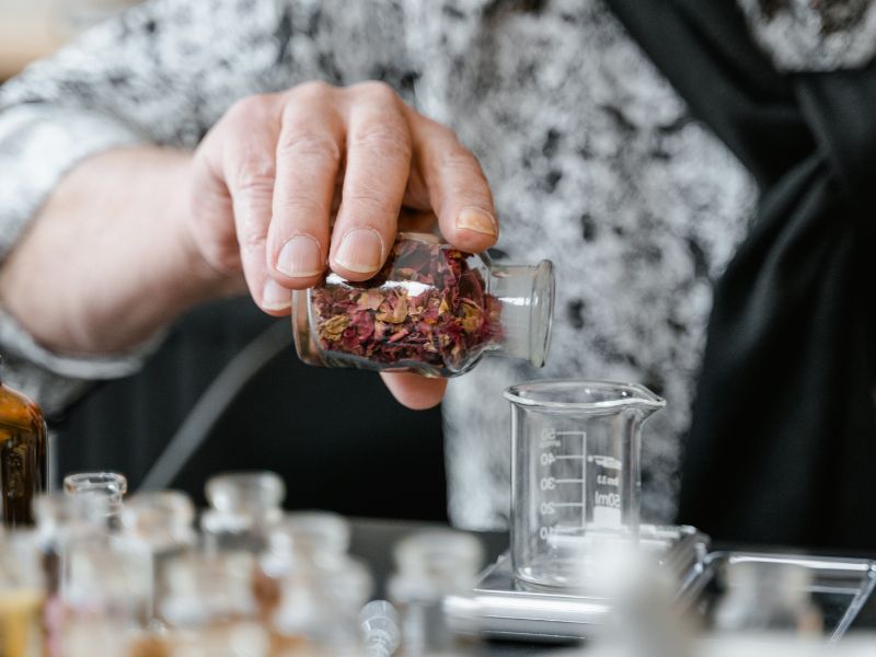 a person pours dried herbs from a glass into a beaker