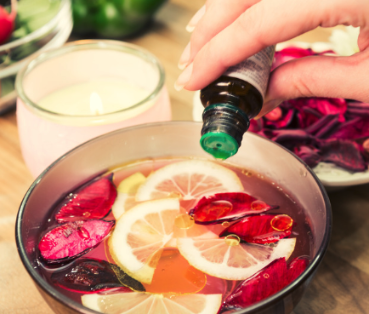 pouring essential oil into a bowl with fruit slices and flower petals