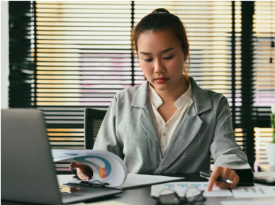 A sits at a desk with a laptop and looks at charts