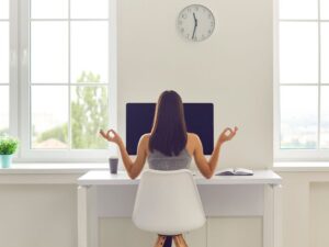 A woman sitting at a desk facing large windows