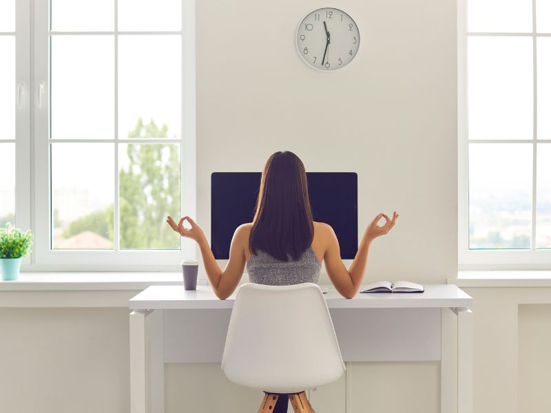 A woman sitting at a desk facing large windows