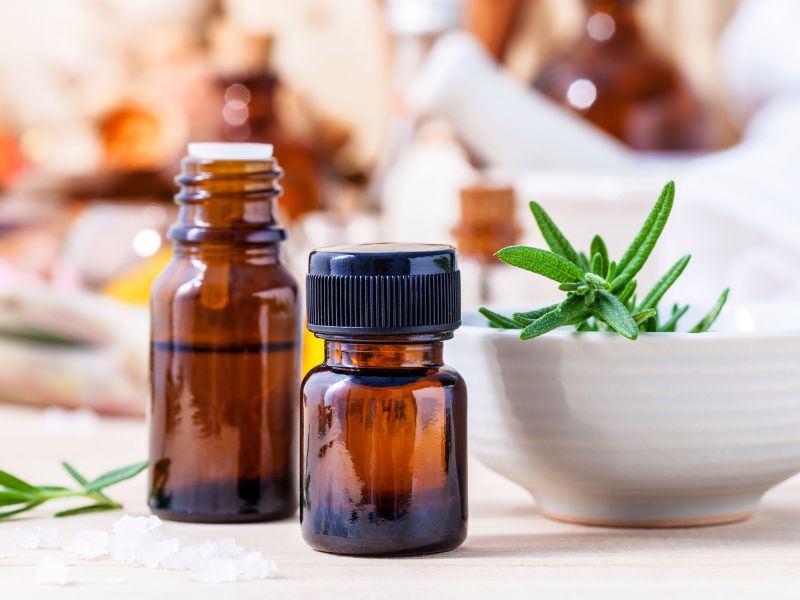 Bottles of essential oils next to a white bowl with green herbs