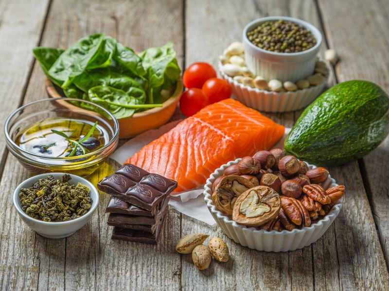 An assortment of healthy foods, including salmon, olive oil, dark chocolate, and avocado