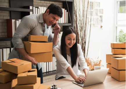 A man and a woman surrounded by boxes look at a laptop
