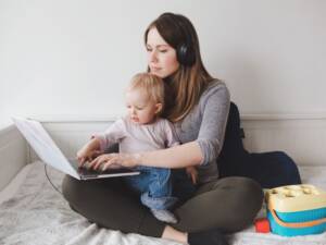 a woman works on a laptop while holding a baby