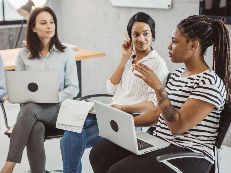 3 women sitting in a circle with laptops and paper