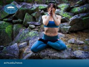 A woman in a cross-legged yoga pose on mossy rocks outdoors