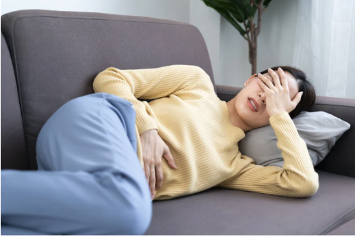 A stressed woman laying on a couch covering her eyes