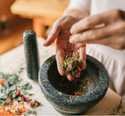Close up of hands sifting through herbs over a mortar and pestle