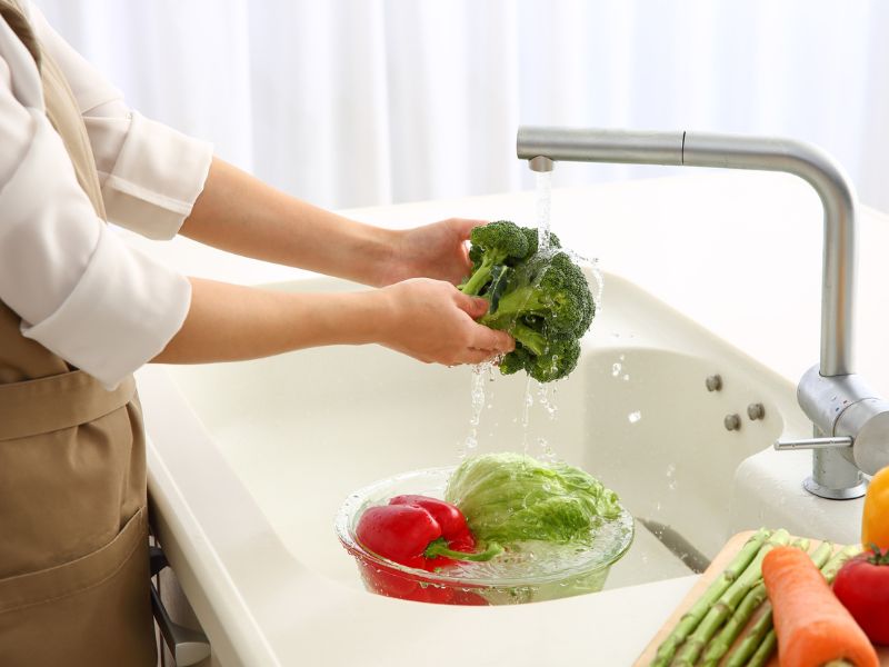 A person washing produce in a kitchen sink