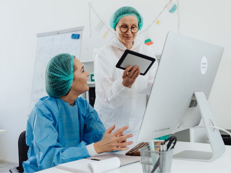 2. Two healthcare professionals in scrubs focused on a computer screen, discussing information.