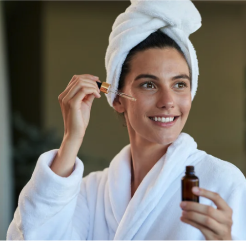 a woman in a bathrobe and towel putting a carrier oil on her skin