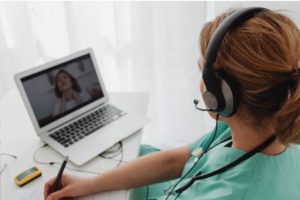 2. A healthcare professional in scrubs operates a laptop while wearing a headset, engaged in a task.