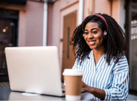 A smiling woman working at a laptop wearing headphones