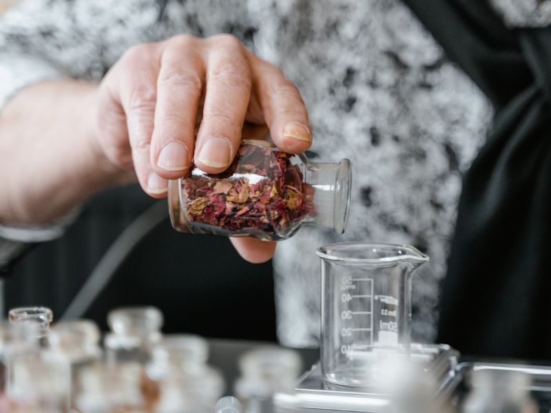 a hand pouring dired herbs from a glass container into a cup on a scale