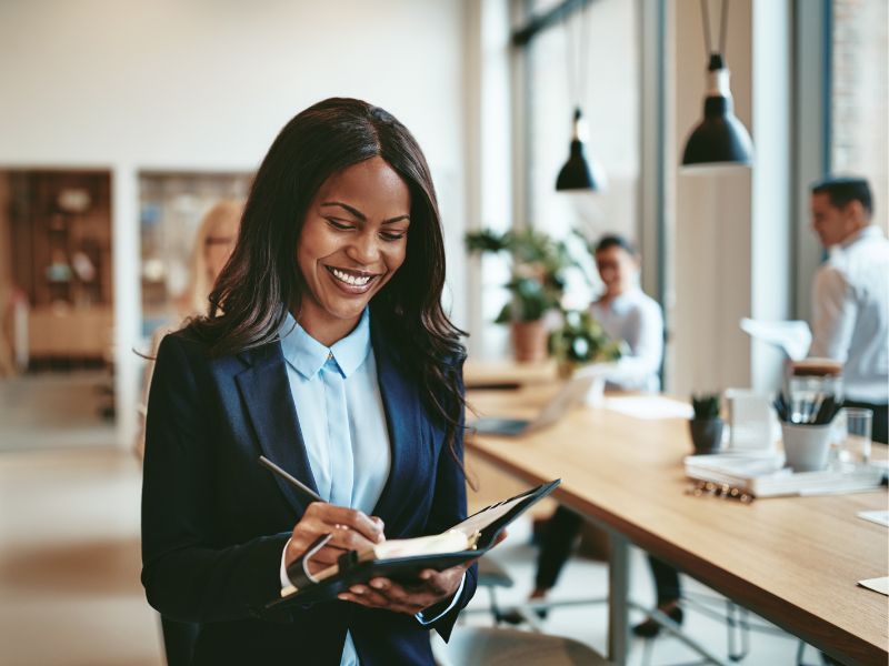 A smiling woman writing in a notepad in an office