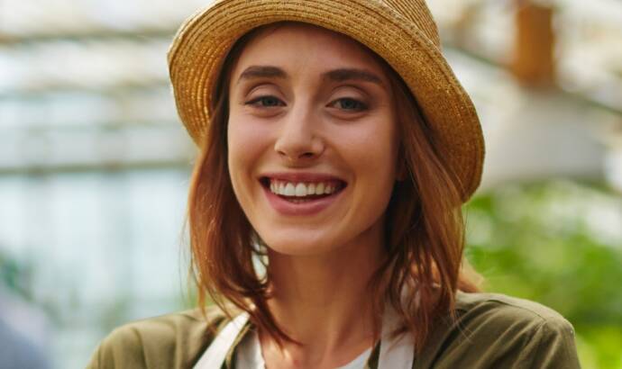 Smiling woman wearing an apron and straw hat in a garden setting.