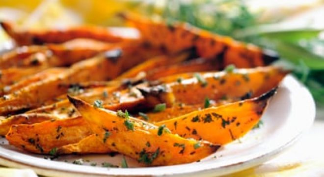 slices of orange vegetables, roasted and covered in herbs, sit on a white plate