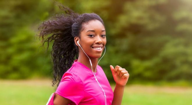 woman with dark curly hair in a ponytail and wearing a pink tshirt runs while looking into the camera