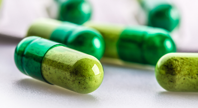 close up shot of pills that are half light green, half dark green with powder inside of them